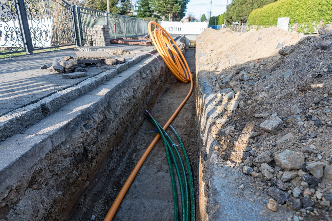LWL Verlegekabel im Erdreich neben Gehweg mit orangefarbenem Leerrohr im Kabelgraben